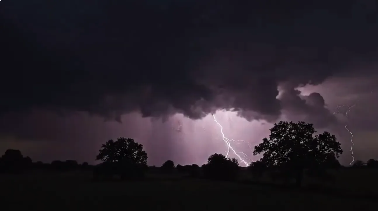 A dark storm spreading over a distant industrial landscape as lightning illuminates the horizon.